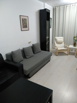 A modern living room with a grey sofa, a black cabinet, a white armchair, and a small table with a vase.
