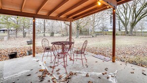 Eine überdachte Terrasse mit Betonboden, Metallstühlen und einem Tisch.