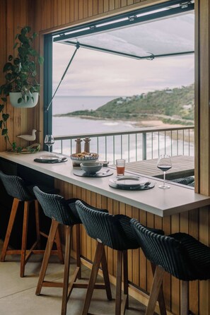 A dining area with a view of the ocean, wooden walls, and a table set with plates, glasses, and a bowl. - At Wye Eyrie II (Wye River)