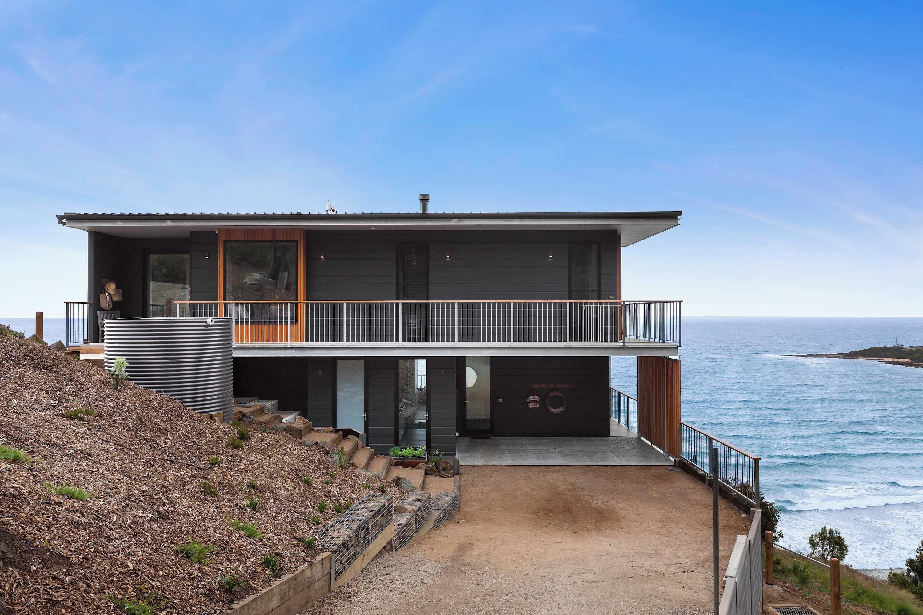 A modern two-story house with a balcony, a garage, and a view of the ocean.