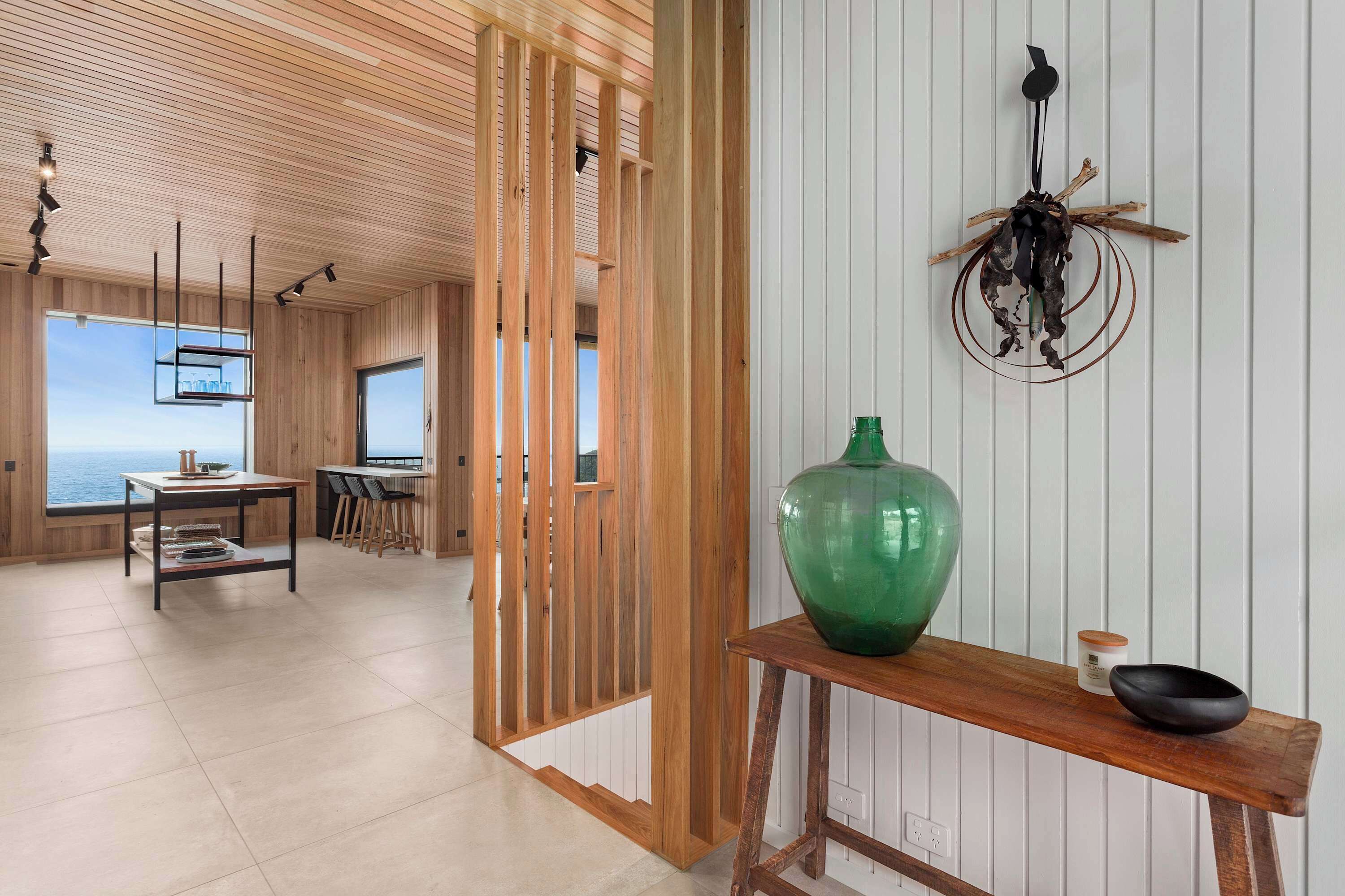 A modern interior with a wooden ceiling, a dining area, a large green vase, and a wall-mounted decoration.