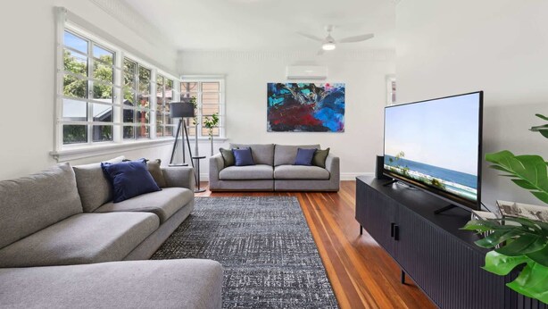 A modern living room with a grey sofa, a black floor lamp, a large abstract painting, a flat-screen TV, and a wooden floor.