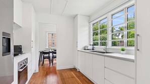A modern kitchen with white cabinetry, a wooden floor, and a large window with multiple panes.