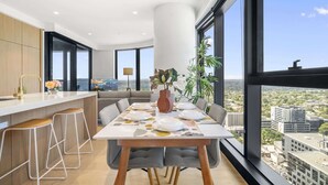 A modern kitchen with a dining area, large windows, and a city view. - High-Rise 3-Bed Apartment with Premium Amenities (Box Hill)