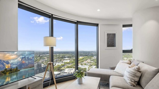 A modern living room with a large window, a flat-screen TV, a lamp, a sofa, and a coffee table. - High-Rise 3-Bed Apartment with Premium Amenities (Box Hill)