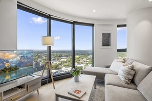 A modern living room with a large window, a flat-screen TV, a lamp, a sofa, and a coffee table. - High-Rise 3-Bed Apartment with Premium Amenities (Box Hill)