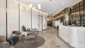 A modern hotel lobby with marble walls, a reception desk, seating area, and a chandelier. - High-Rise 3-Bed Apartment with Premium Amenities (Box Hill)
