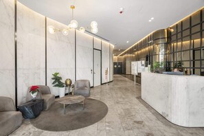 A modern hotel lobby with marble walls, a reception desk, seating area, and a chandelier.