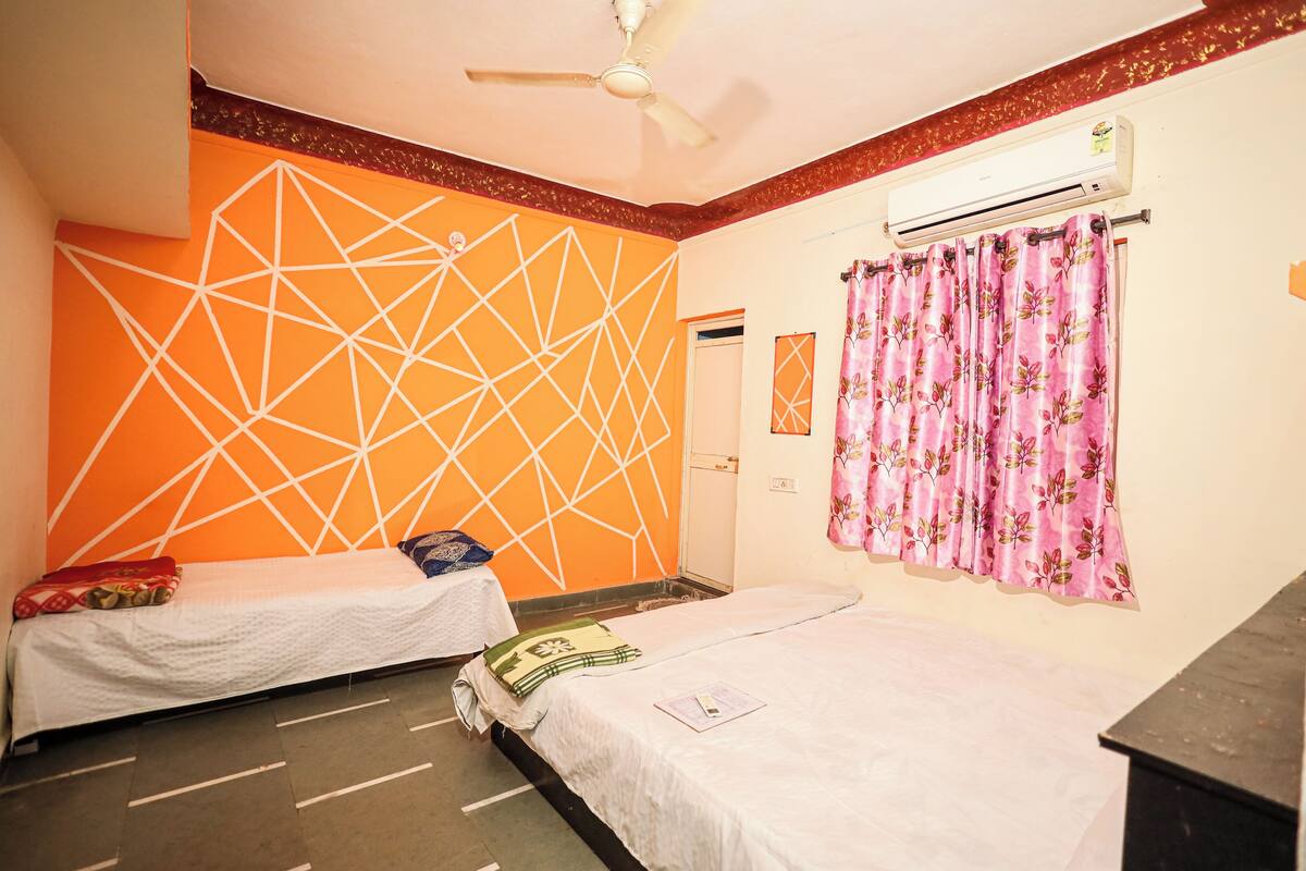 A room with two beds, an air conditioning unit, a ceiling fan, and a window with floral curtains.
