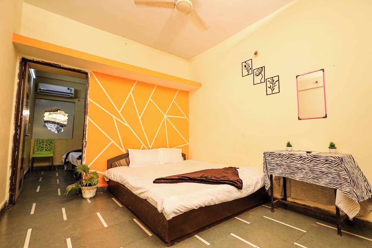A bedroom with a bed, a small table with a zebra-patterned tablecloth, a ceiling fan, and a wall with geometric patterns and framed pictures.
