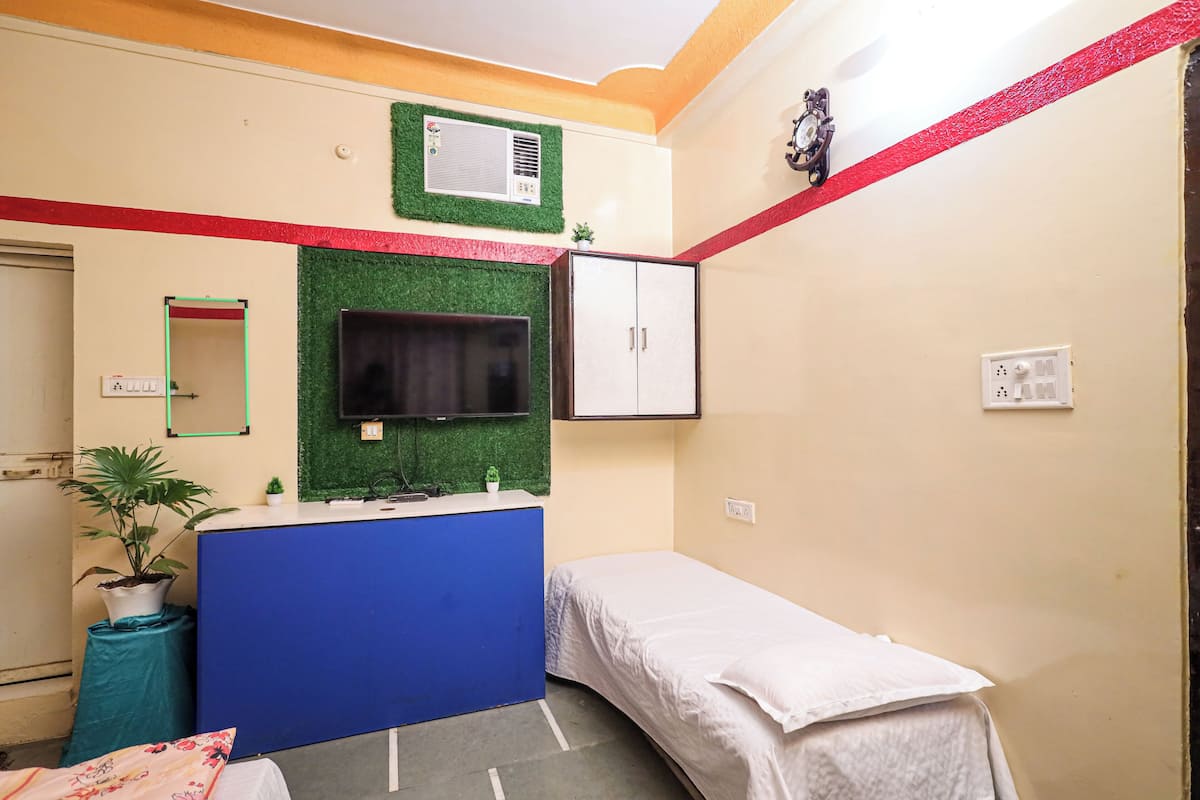A small, compact room with a bed, a desk with a chair, a television, and a wardrobe.