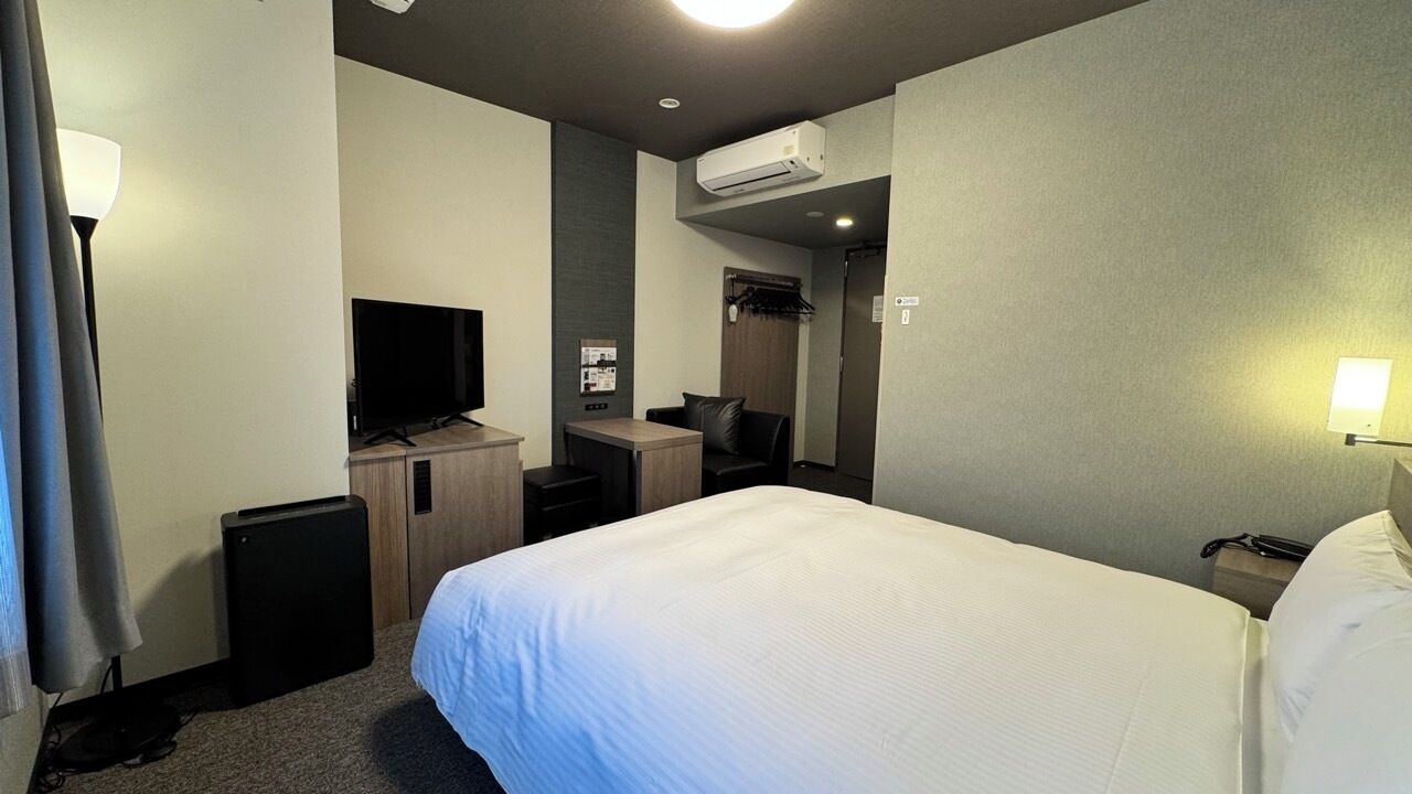 Una habitación de hotel con cama, escritorio, televisor y aire acondicionado.