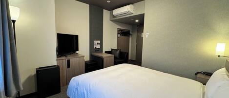 Una habitación de hotel con cama, escritorio, televisor y aire acondicionado.