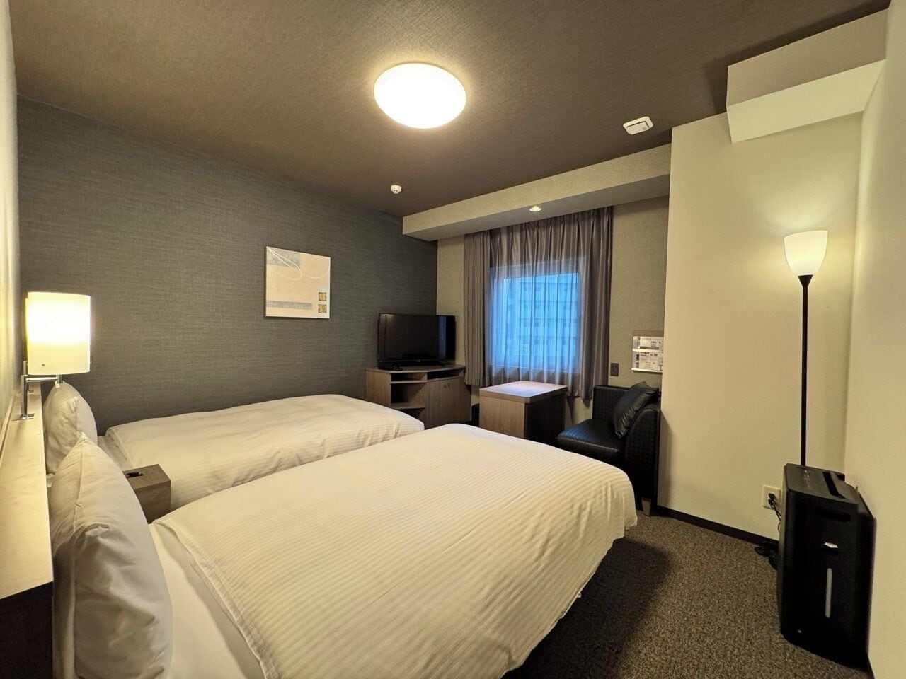 Ett hotellrum med två sängar, ett skrivbord, en stol, en tv och en lampa.
