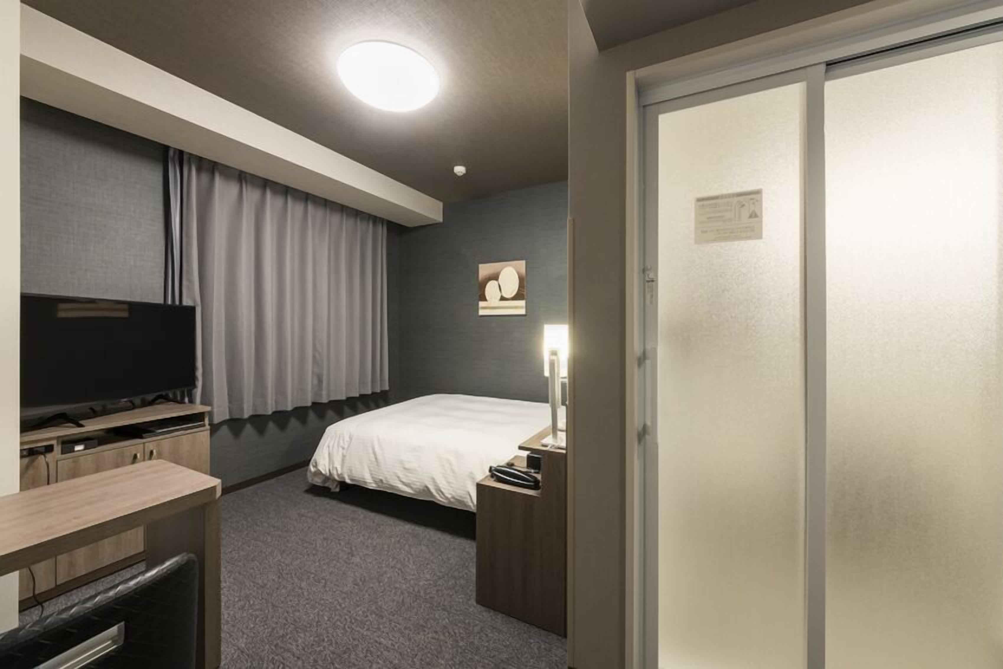 A hotel room with a bed, a desk, a television, a nightstand, and a wardrobe.