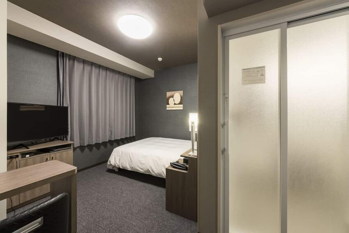 A hotel room with a bed, a desk, a television, a nightstand, and a wardrobe.