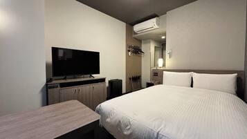 Una habitación de hotel con cama, escritorio, televisión, aire acondicionado y espejo.