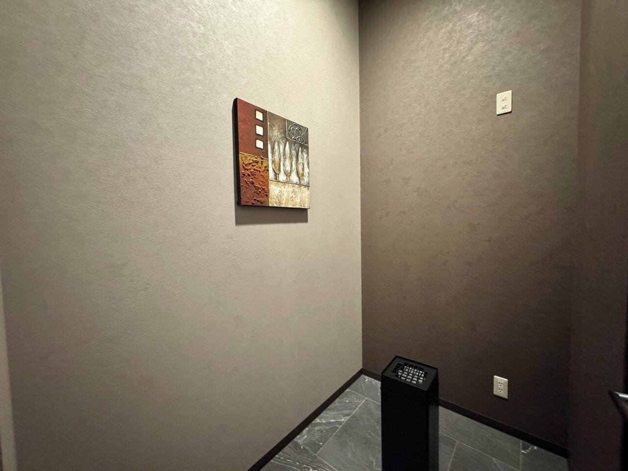 Un couloir avec un mur à texture, un petit tableau et un haut-parleur noir.