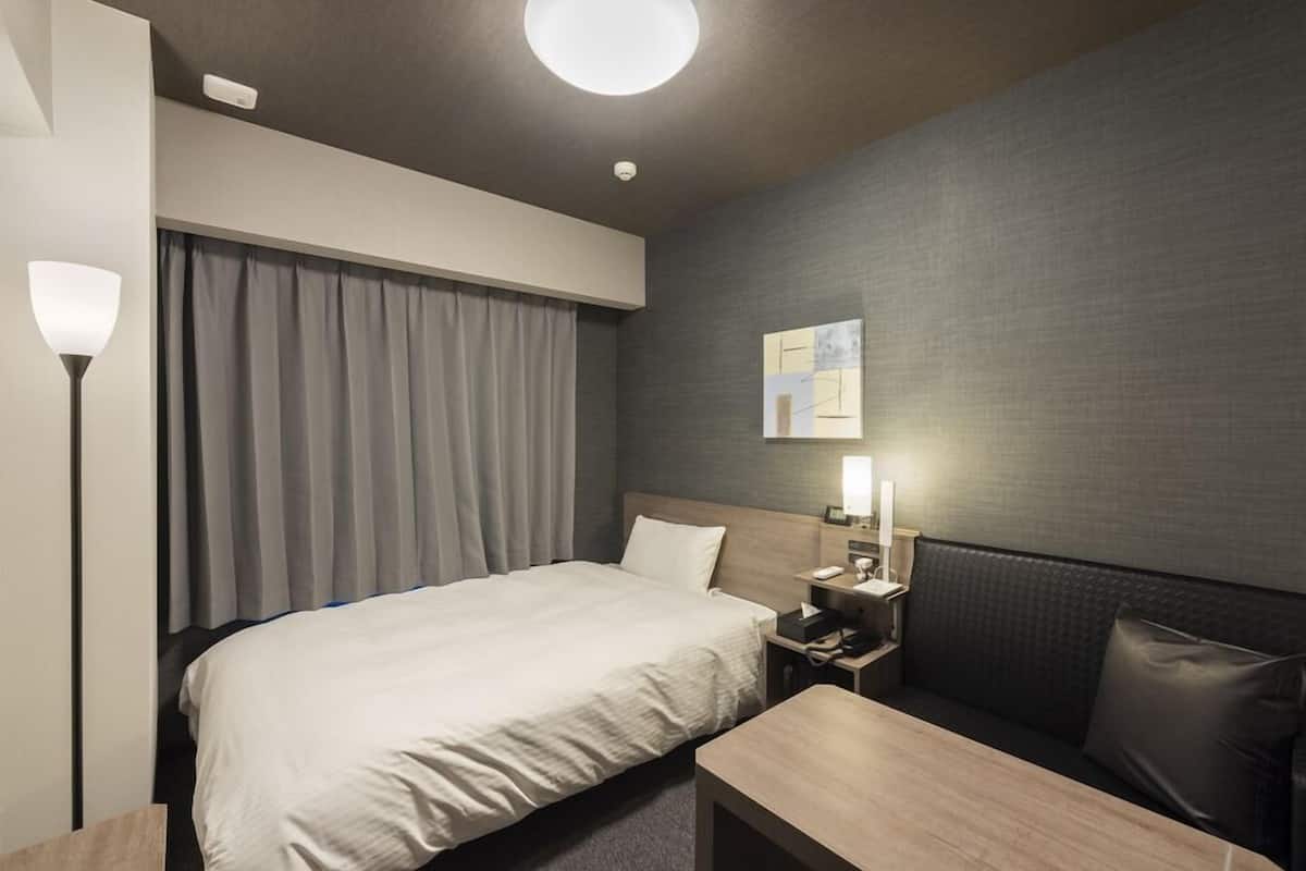 A modern hotel room with a bed, bedside table, lamp, and a small seating area.
