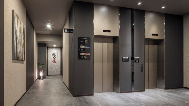 A modern elevator area with two elevators, a digital display, and a wall-mounted information panel. - HOTEL ROUTE-INN Grand NAGOYA FUJIGAOKA EKIMAE (Nagoya)