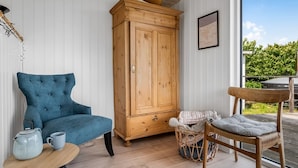 A cozy room with a blue upholstered chair, a wooden cabinet, a wicker chair, and a small table with a teapot and cup. - "Shaya" - 325m from the sea by Interhome (Allingåbro)