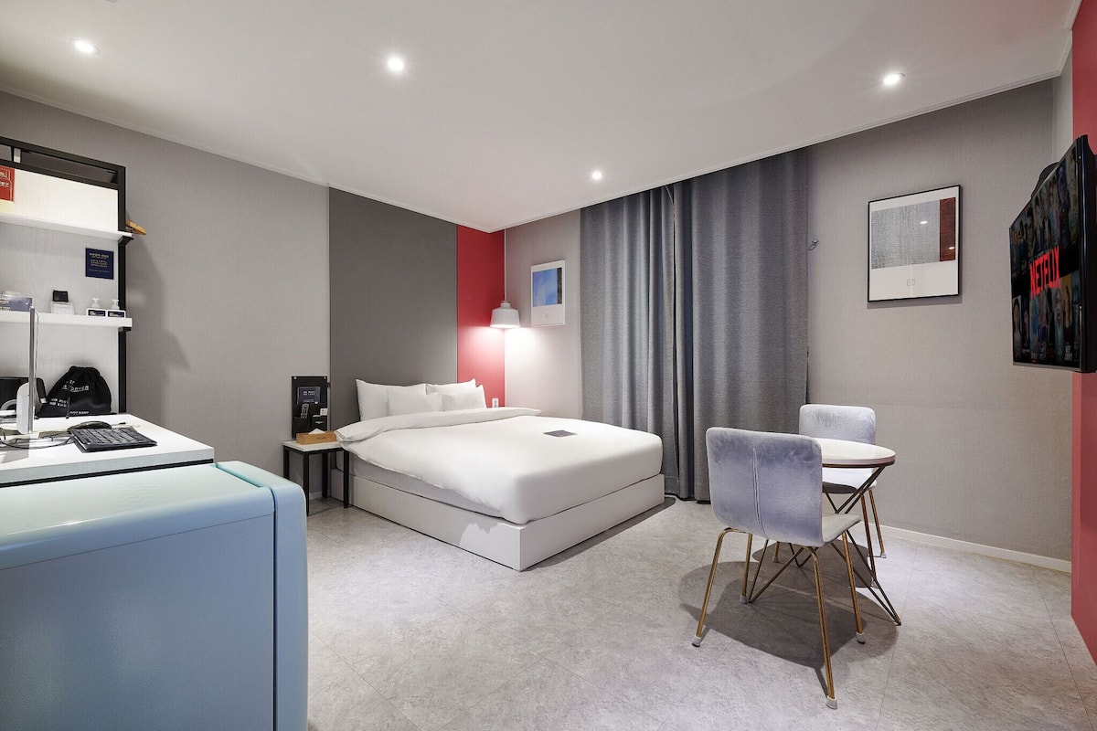 A modern hotel room with a bed, desk, chair, and a small table.