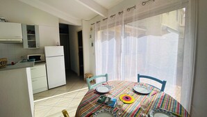 A dining area with a round table set for two, a refrigerator, and a kitchen area with cabinets and a microwave. - 🌼 Villa aux Capellans with terrace and pool 🌼 (Saint-Cyprien)