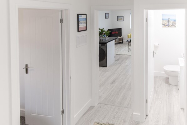 A hallway leading to a living area with a TV, a washing machine, and a dining area.