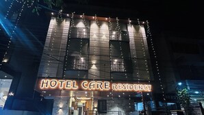 A building with a sign reading "HOTEL CARE RESIDENCY" at night, featuring a modern design with illuminated windows and string lights. - Hotel Care Residency (Indore)