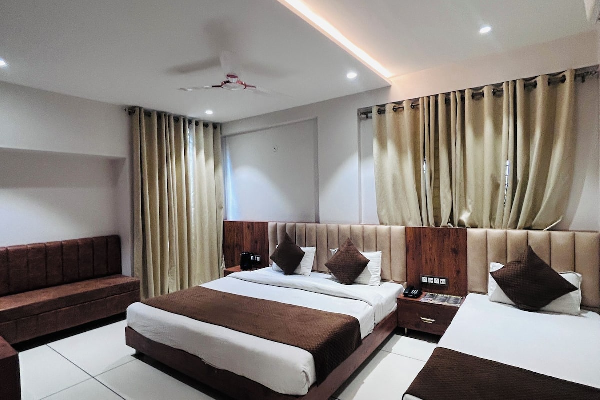 A modern hotel room with a large bed, a sofa, a bedside table, and a ceiling fan.