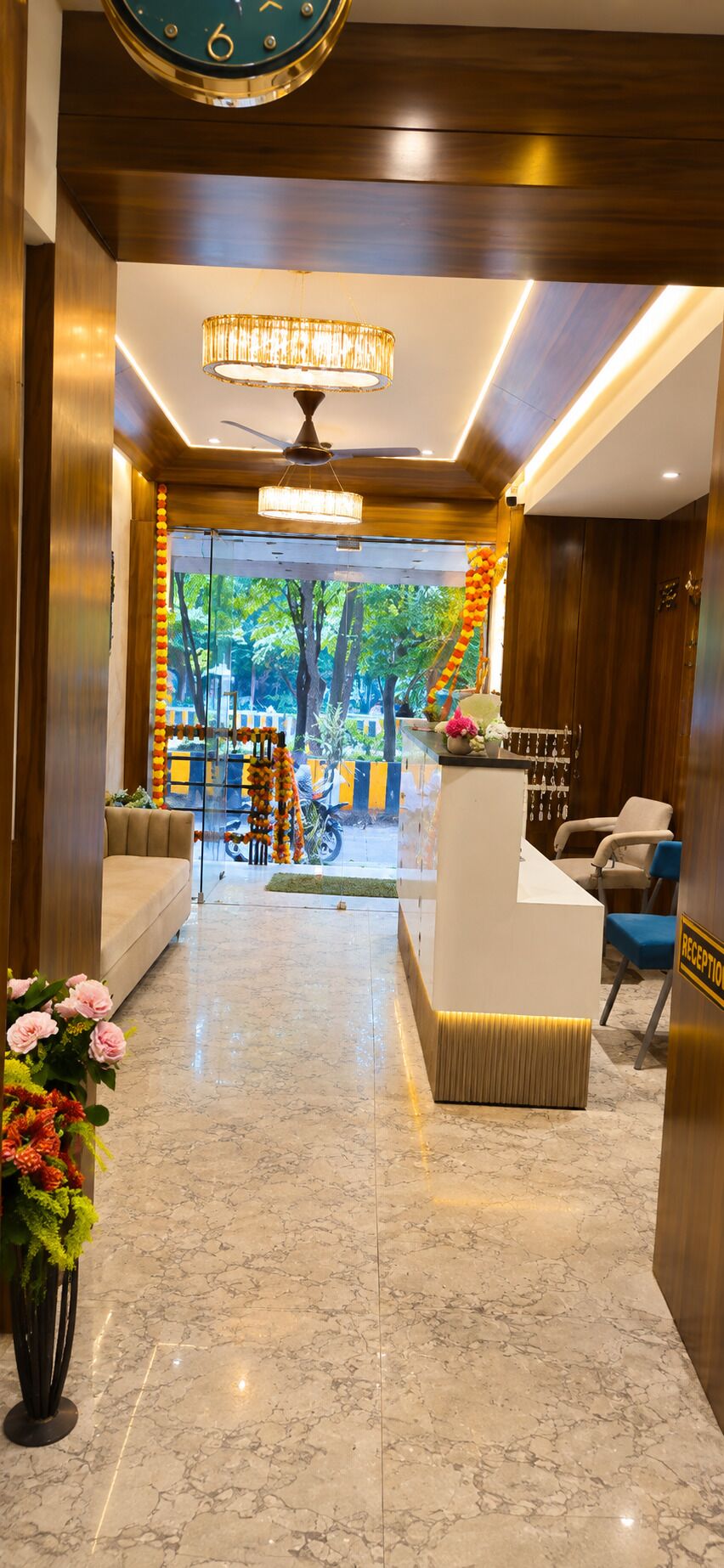 Zona de recepción de un hotel con suelo de mármol, mostrador de recepción, sofá y ventilador de techo.