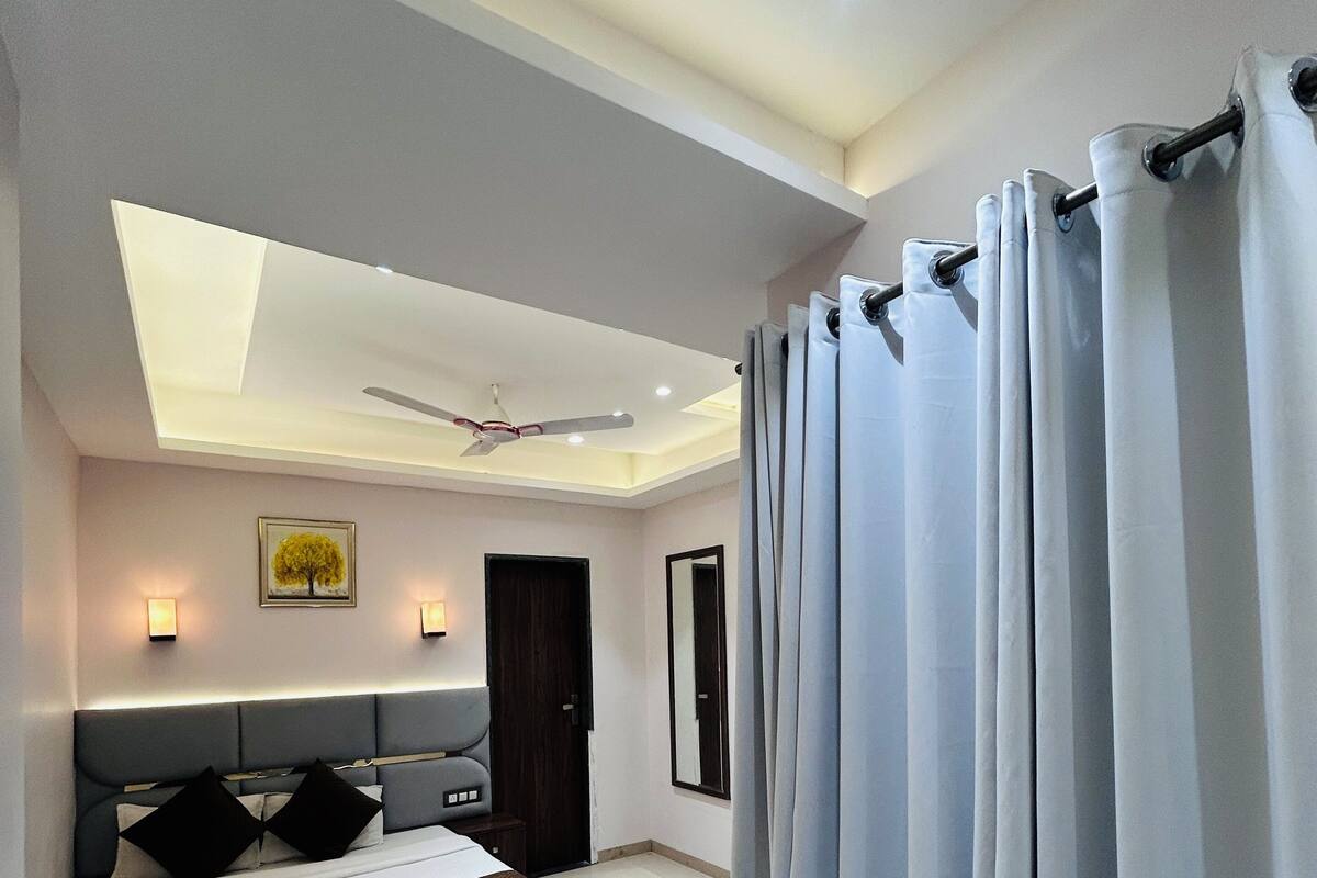 A modern bedroom with a large bed, a sofa, a ceiling fan, and a skylight.