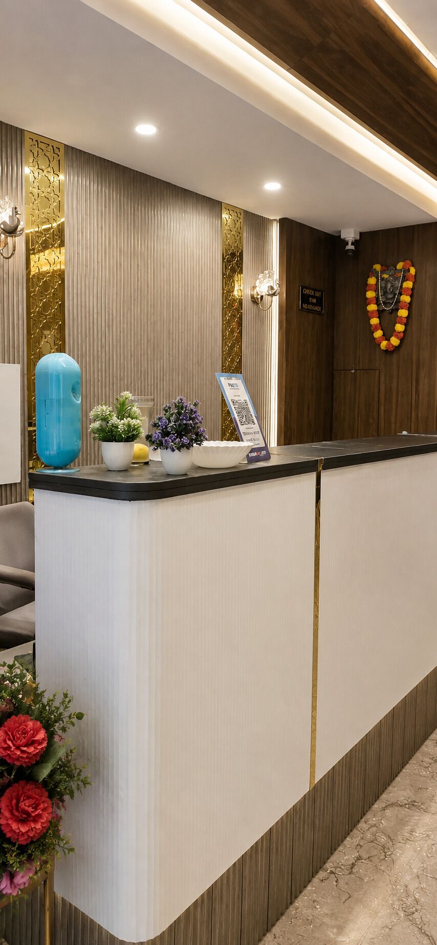 A reception desk with a check-in counter, a blue decorative object, potted plants, and a sign with a QR code.
