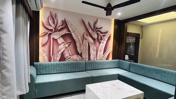A modern living room with a sectional sofa, a marble coffee table, and a decorative wall with leaf patterns. - Hotel Care Residency (Indore)