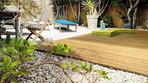 Una terraza de madera con sillones de lounge y un cojín verde pequeño.