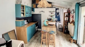 Cocina compacta con armarios verde azulado, encimera de madera y lámpara colgante.