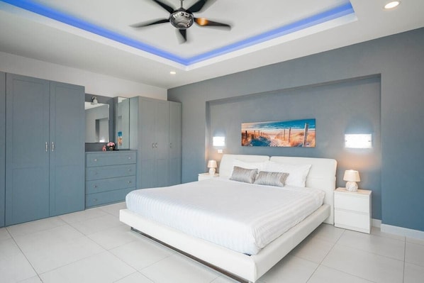 A bedroom with a bed, nightstands, a ceiling fan, and a painting on the wall.