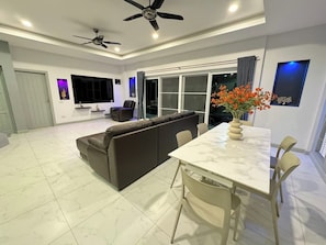 A modern living room with a sectional sofa, a dining table with chairs, a ceiling fan, and a large window.