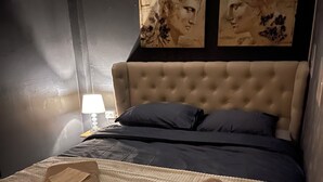 Un lit bien fait, avec une tête de lit beige et une literie bleu foncé, une serviette pliée posée sur le lit, et deux œuvres d’art encadrées accrochées au mur au-dessus du lit.