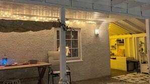 Un espace extérieur accueillant, recouvert de neige, avec une table et des chaises, une lanterne et une sculpture décorative représentant un personnage de neige.