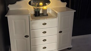 Une coiffeuse blanche avec un miroir, deux bougies allumées et un petit vase de fleurs.
