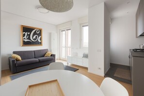 A modern living room with a sofa, a dining table, and a kitchen area.