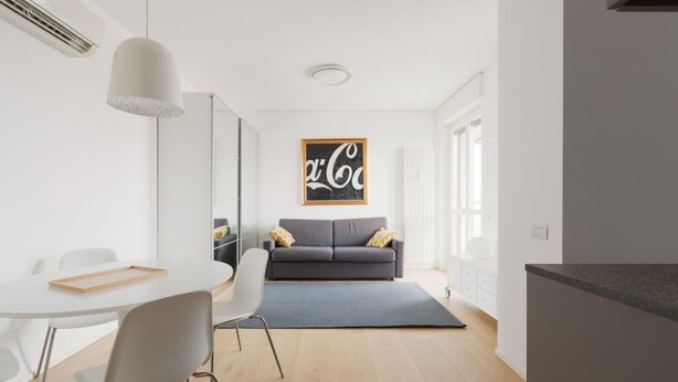 En moderne stue med en grå sofa, hvide stole, et spisebord og et stort kunstværk på væggen.