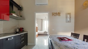 A modern kitchen with a red cabinet, a dining area with a floral tablecloth, and a hallway leading to a bedroom. - GuestHost - Bright APT with balcony- Milan Piazzale Loreto (Milano)