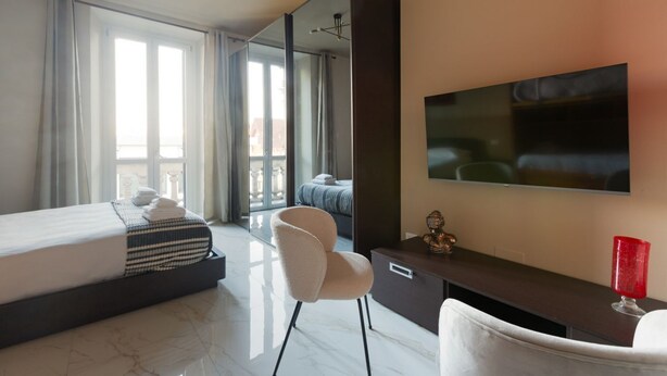 A modern hotel room with a bed, a seating area, a large mirror, a TV, and a balcony with curtains. - GuestHost - Bright APT with balcony- Milan Piazzale Loreto (Milano)
