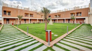 A courtyard with a central fountain, surrounded by a brick building with multiple balconies and a well-maintained lawn. - Citrus Classic Resorts & Spa Mahabalipuram ECR (Cheyyur)