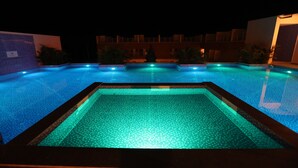 A nighttime swimming pool with a tiled edge and a central rectangular section. - Citrus Classic Resorts & Spa Mahabalipuram ECR (Cheyyur)