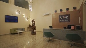A reception area with a modern design, featuring a reception desk, two green chairs, a large wall-mounted clock, and a decorative sculpture. - Citrus Classic Resorts & Spa Mahabalipuram ECR (Cheyyur)