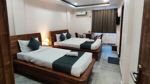 Habitación de hotel con dos camas de madera, un ventilador de techo, una mesita con una silla y un televisor montado en la pared.
