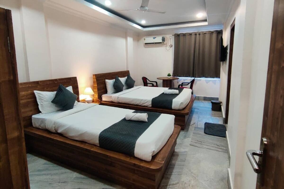 A hotel room with two wooden beds, a ceiling fan, a small table with a chair, and a TV mounted on the wall.